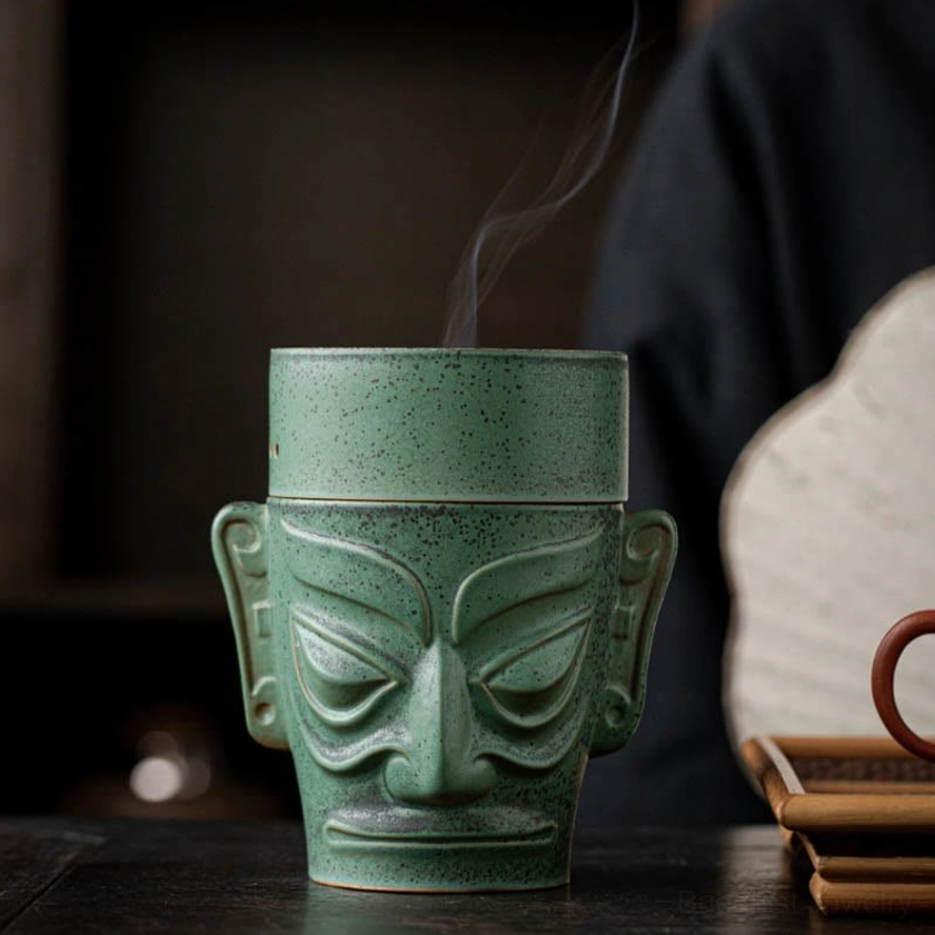 Direct front view of ceramic mask incense burner with subtle rising smoke, classic stylized mask design with speckled green finish