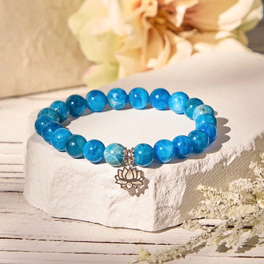 Handmade apatite lotus bracelet styled with dried flowers on stone stand, highlighting the blue gemstone beads and hollow silver lotus charm