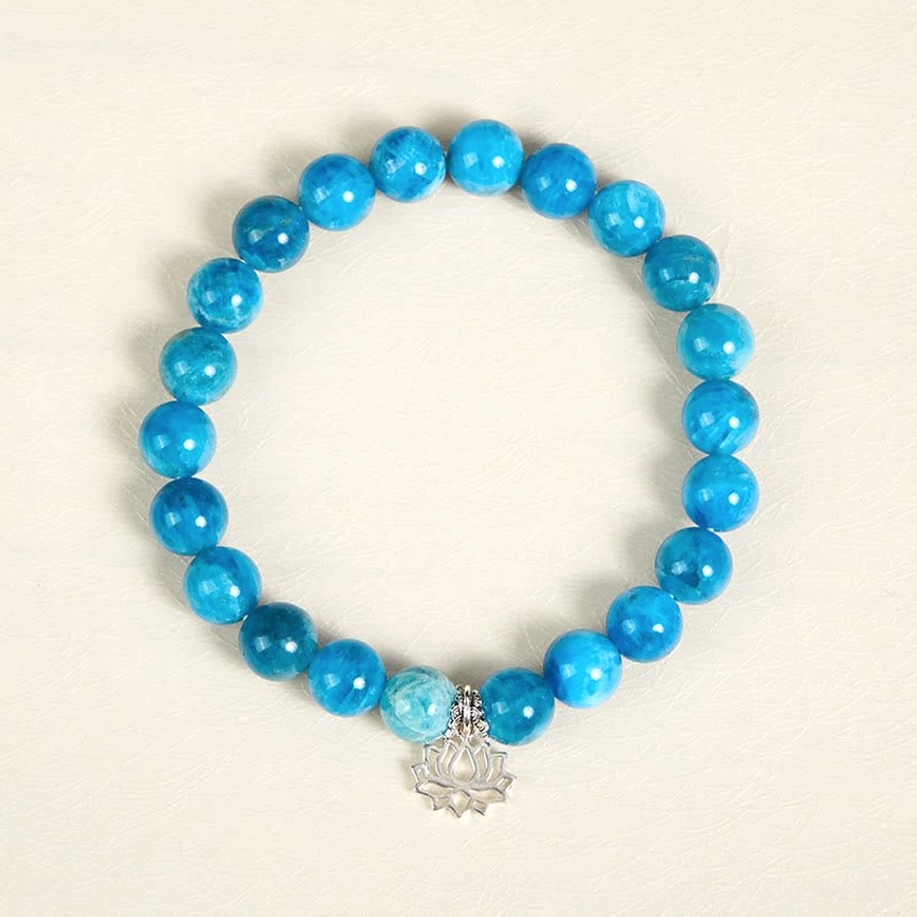 Full view of natural apatite lotus bracelet laid flat, showing complete beaded loop with blue round stones and sterling silver lotus pendant
