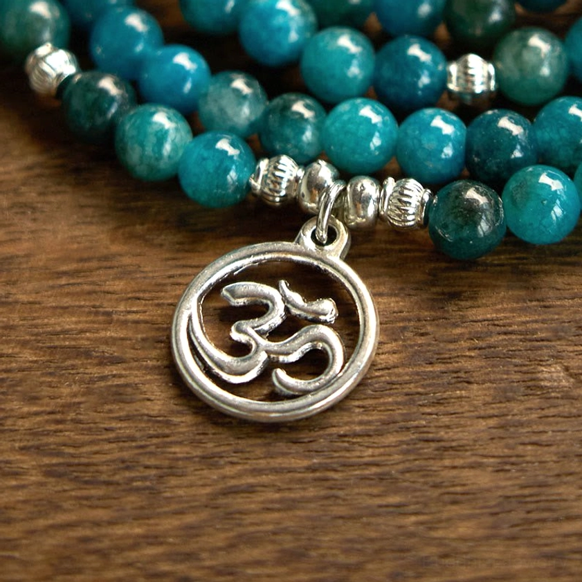 Macro close-up of apatite mala bracelet components showing smooth blue beads, silver spacers, and detailed Om charm pendant