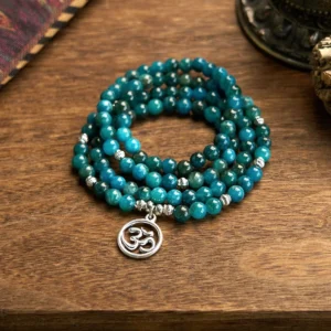 Apatite mala bracelet with Om pendant, 108 beads, teal blue round beads with silver metal accents, top-down overhead view on wooden desktop
