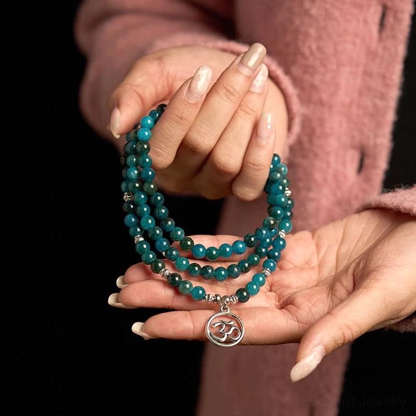 Apatite meditation bracelet two-hand palm display with coiled beaded strands and silver Om pendant on dark studio background