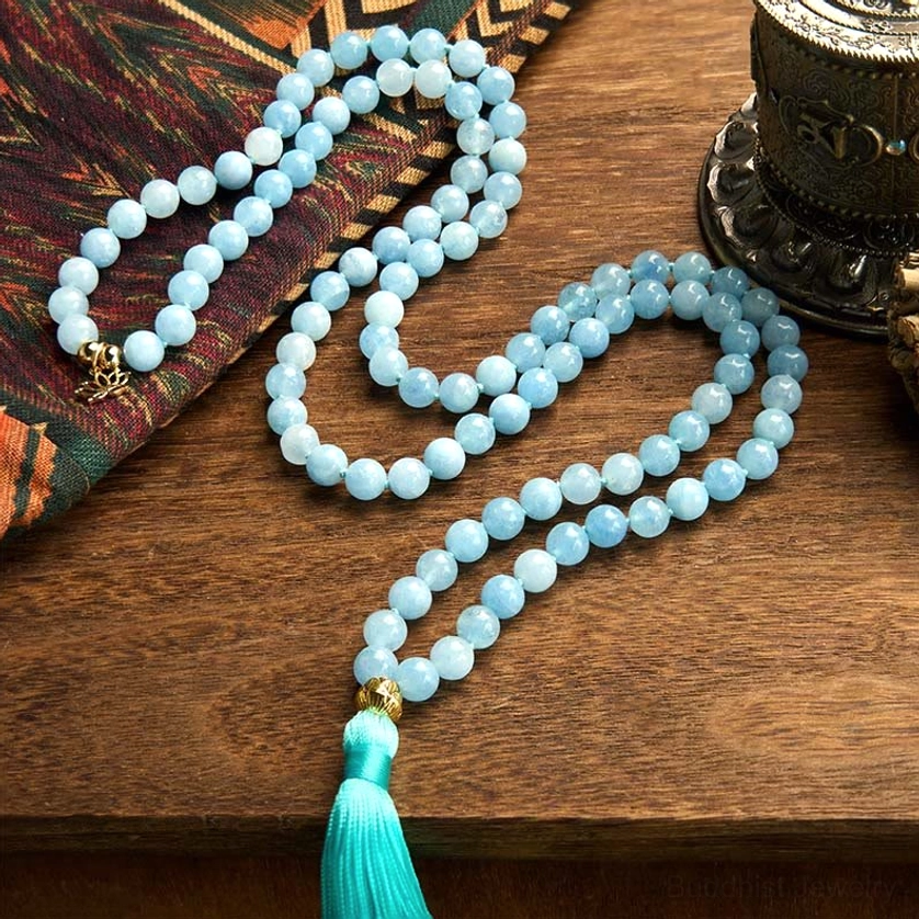 Aquamarine mala prayer beads necklace displayed on patterned fabric with metal lotus charm