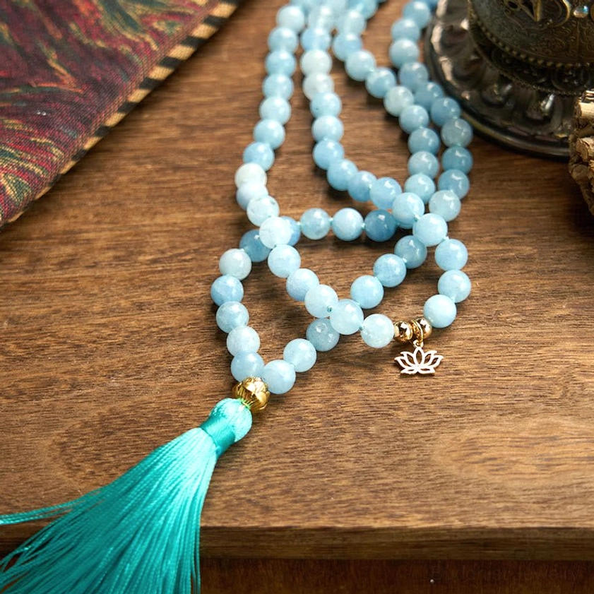 Aquamarine mala prayer beads loosely arranged on vintage wooden table with turquoise tassel
