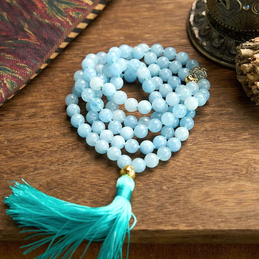 Aquamarine 108 mala prayer beads bracelet coiled on wooden table with turquoise tassel