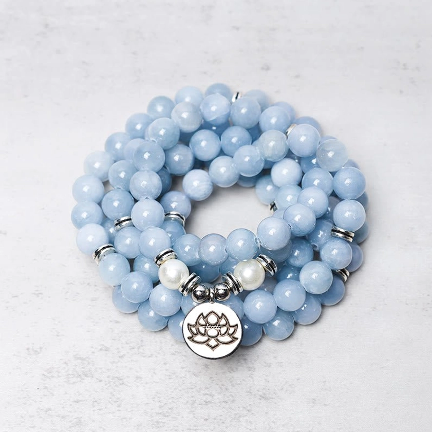 108 aquamarine mala bead bracelet overhead view with silver lotus charm on light background
