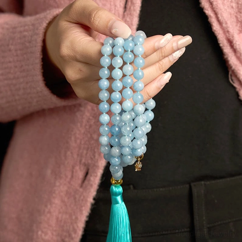 Close-up handheld aquamarine mala bracelet worn showing turquoise tassel size reference