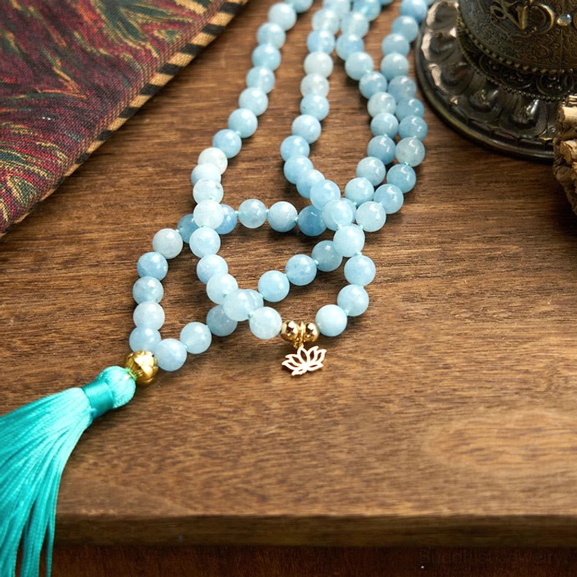 Aquamarine mala prayer beads bracelet flat lay on patterned fabric with lotus charm visible