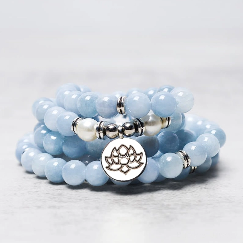 Stacked aquamarine mala bead bracelet close-up showing light blue crystals with white spacer beads and silver lotus charm