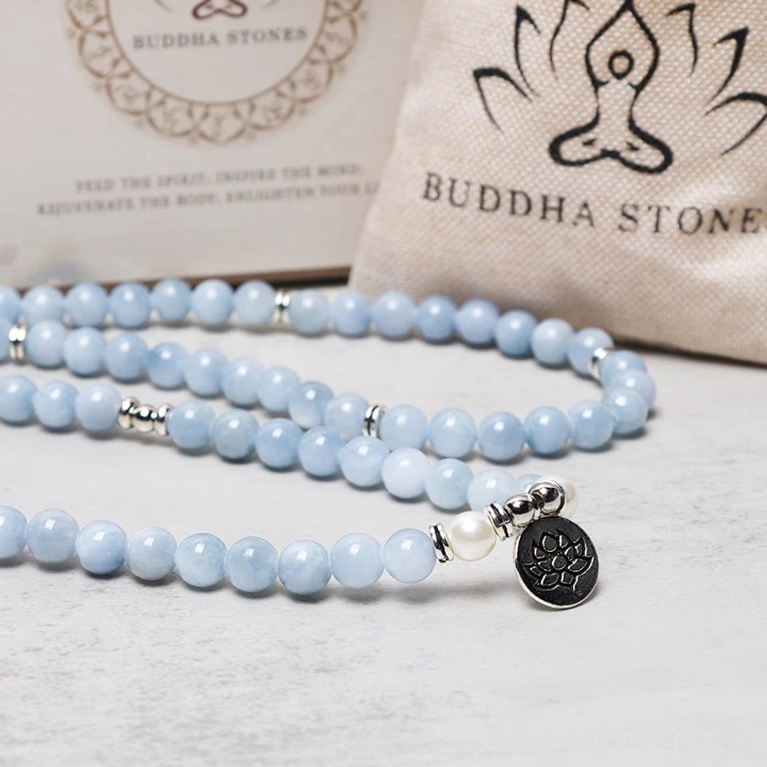 Aquamarine mala bracelet with silver clasp and black lotus charm pendant on branded packaging