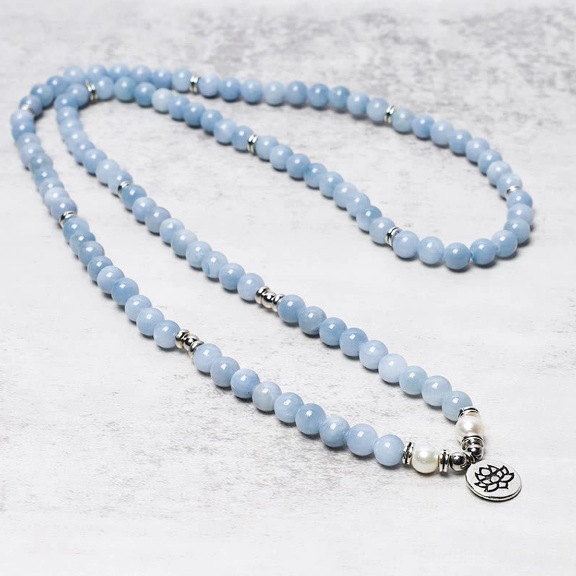 Aquamarine mala prayer bead necklace flat lay with silver metal accents and lotus pendant
