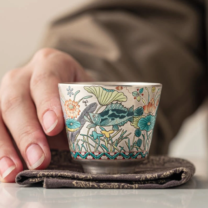 Artisan holding ceramic gongfu tea cup with fish and lotus design, close-up view