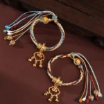 Handmade auspicious cloud lock bracelet with healing symbols and protective bells, multicolor braided cord with antique gold hardware on dark wooden surface