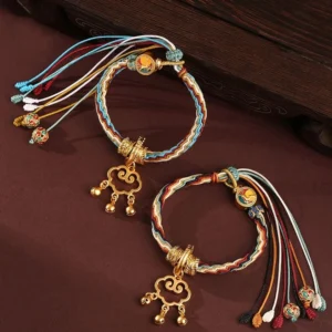 Handmade auspicious cloud lock bracelet with healing symbols and protective bells, multicolor braided cord with antique gold hardware on dark wooden surface