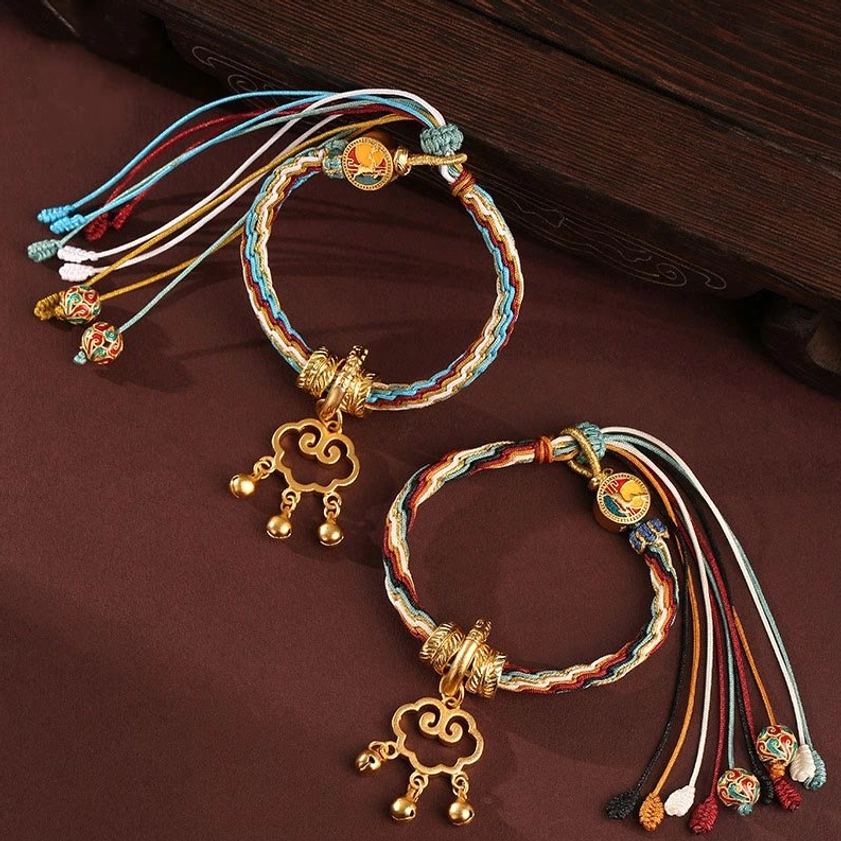 Handmade auspicious cloud lock bracelet with healing symbols and protective bells, multicolor braided cord with antique gold hardware on dark wooden surface