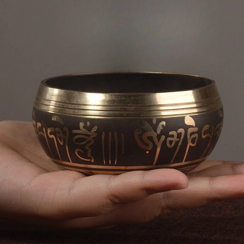 Side view of handcrafted Buddhist singing bowl in palm showing gold sacred scripture patterns and polished gold-trimmed rim