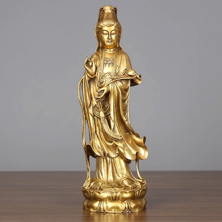 Golden Avalokitesvara brass statue frontal view on wooden desk, showing detailed lotus base and flowing robes with warm polished finish
