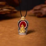 Avalokitesvara Dzi bead copper pendant necklace with gold Buddha statue, red enamel inlay, and turquoise accents on wooden background