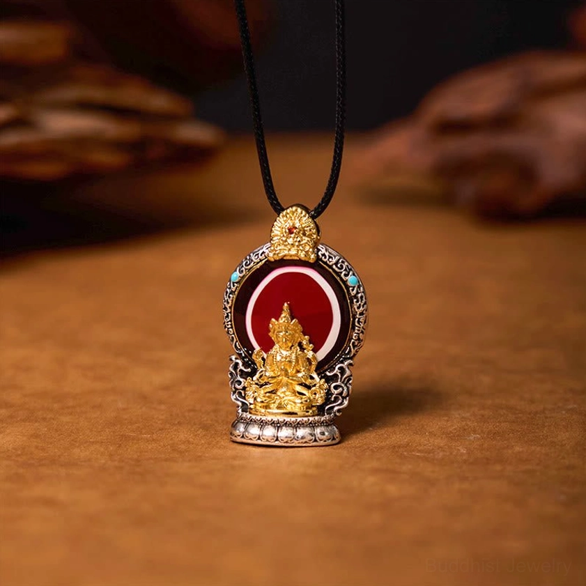 Avalokitesvara Dzi bead copper pendant necklace with gold Buddha statue, red enamel inlay, and turquoise accents on wooden background