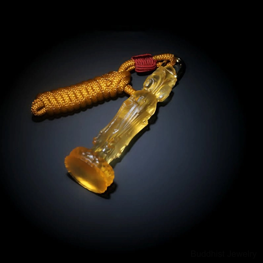 Avalokitesvara Buddhist glass pendant with braided cord laid flat, top-down view on dark background