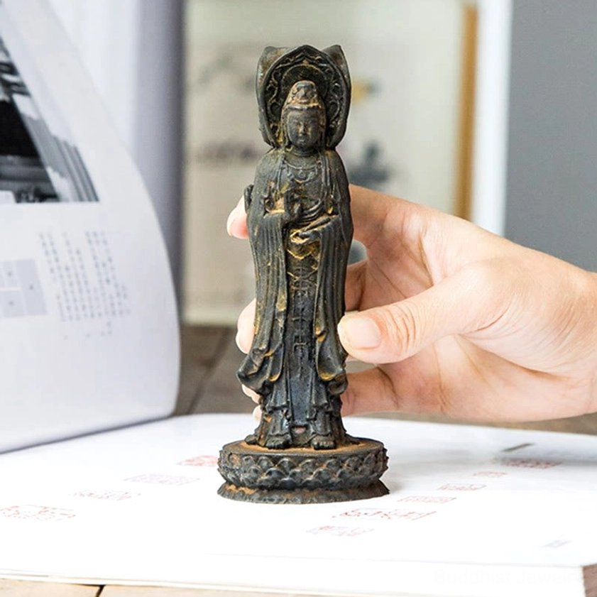Hand holding three-faced Avalokitesvara statue displayed on open book with lotus base