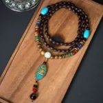 Avalokitesvara coconut shell mala necklace flat lay with turquoise Buddha pendant and natural wooden beads on dark background