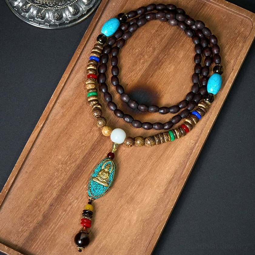 Avalokitesvara coconut shell mala necklace flat lay with turquoise Buddha pendant and natural wooden beads on dark background