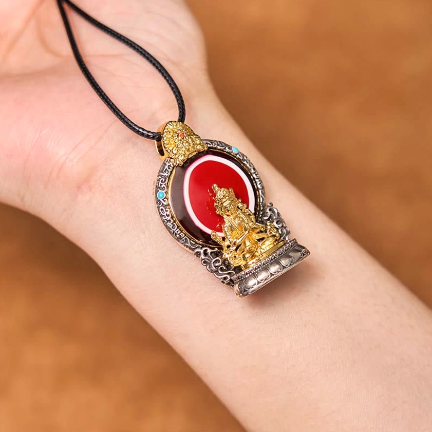 Avalokitesvara copper pendant necklace worn on wrist showing side view with black cord and detailed metal casing with red inlay