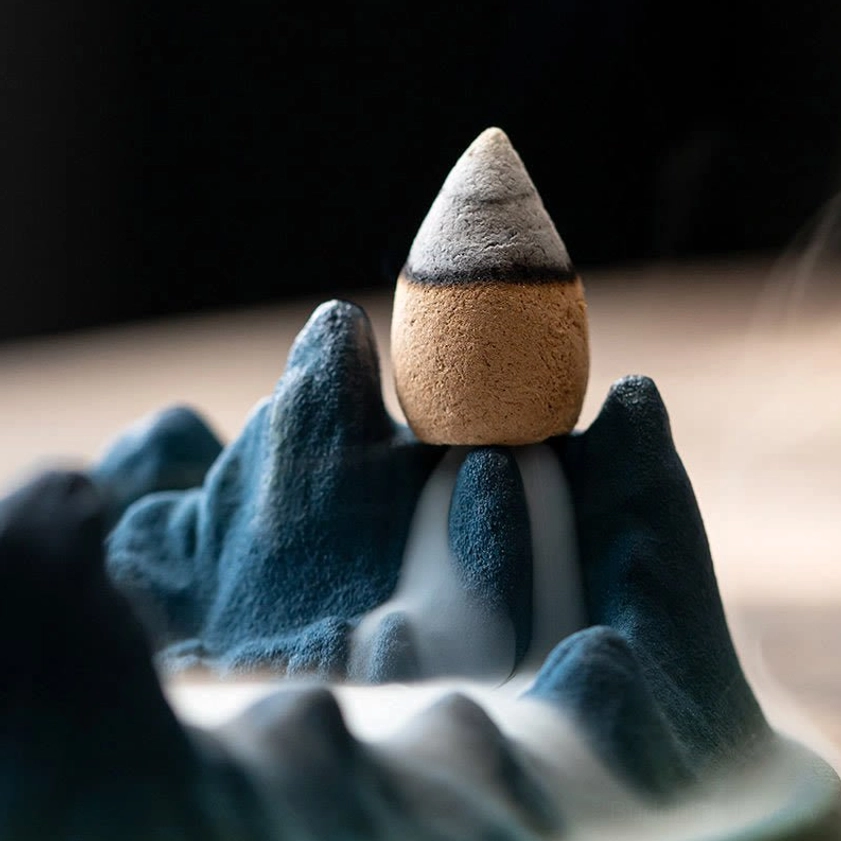 Low side angle of Buddhist ceramic incense burner with incense cone installed, showing mesmerizing backflow smoke flowing down mountain design