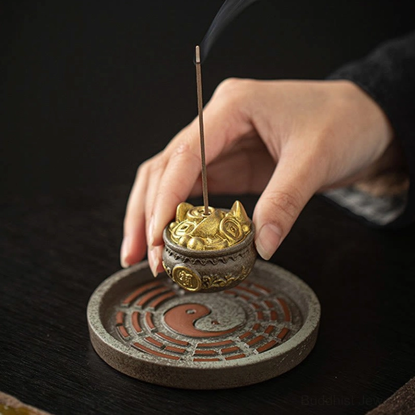 Three-quarter view of brown ceramic Bagua incense burner with gold treasure bowl and hands positioning lit incense