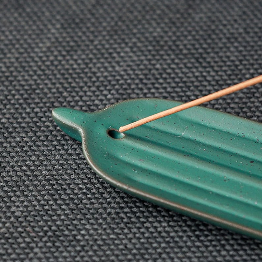 Green striped ceramic bamboo leaf incense tray with incense stick inserted on dark placemat