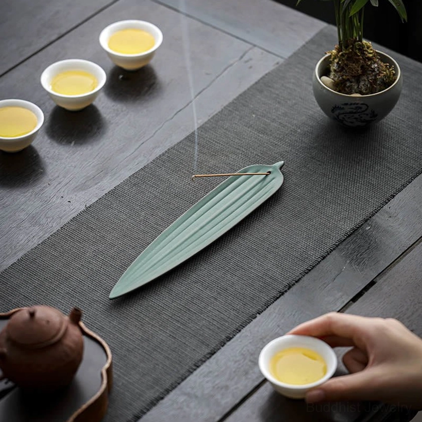 Buddhist meditation incense burner with burning incense near tea set and potted plant on table