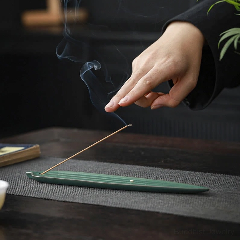 Close-up overhead of green ribbed ceramic bamboo leaf incense tray with hand adjusting incense stick