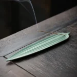 Dark green bamboo leaf ceramic incense burner with burning incense and rising smoke on wooden tea table