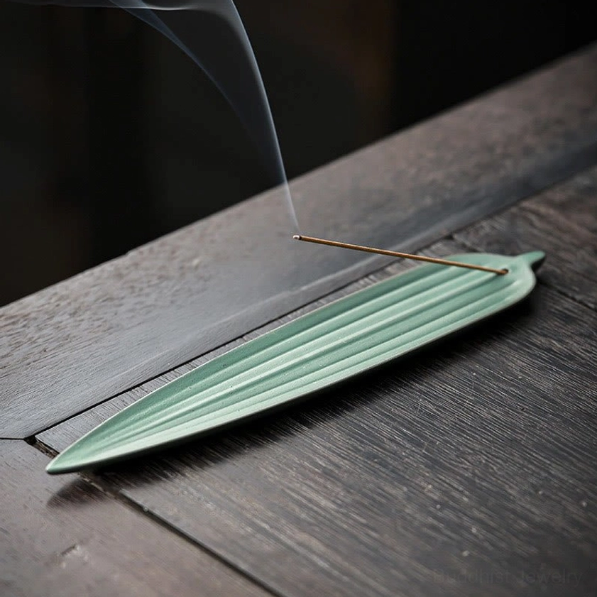 Dark green bamboo leaf ceramic incense burner with burning incense and rising smoke on wooden tea table