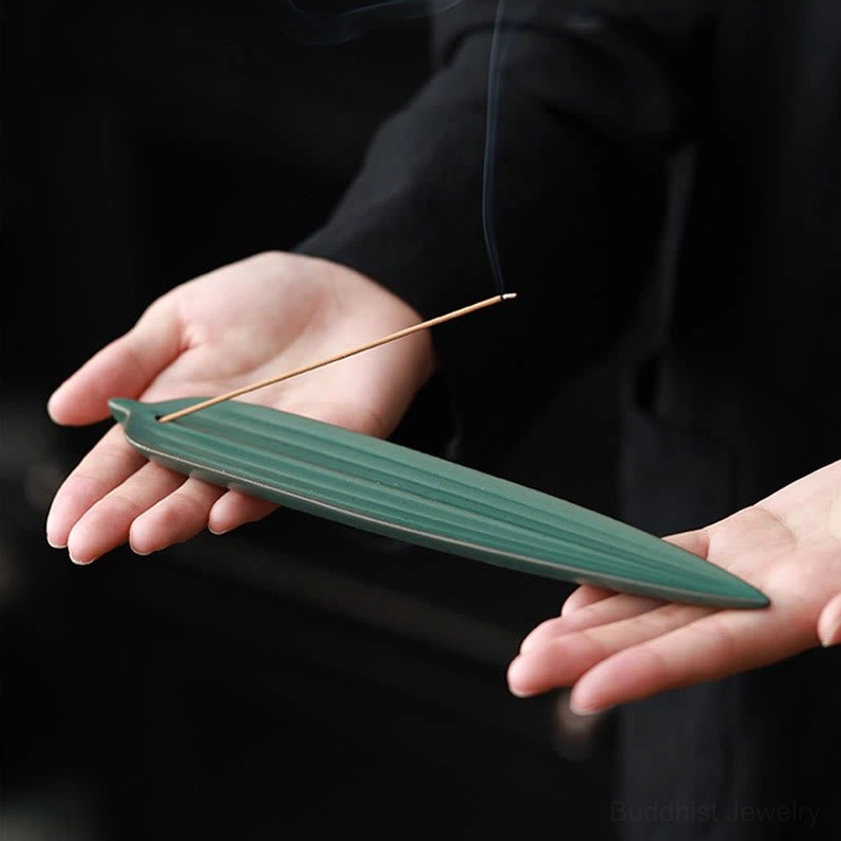 Hands holding burning bamboo leaf ceramic incense burner with smoking incense stick