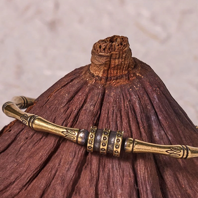 Close-up side view of antique brass bamboo lotus bangle featuring engraved lotus flower details and decorative metal hardware, styled with dried lotus pod