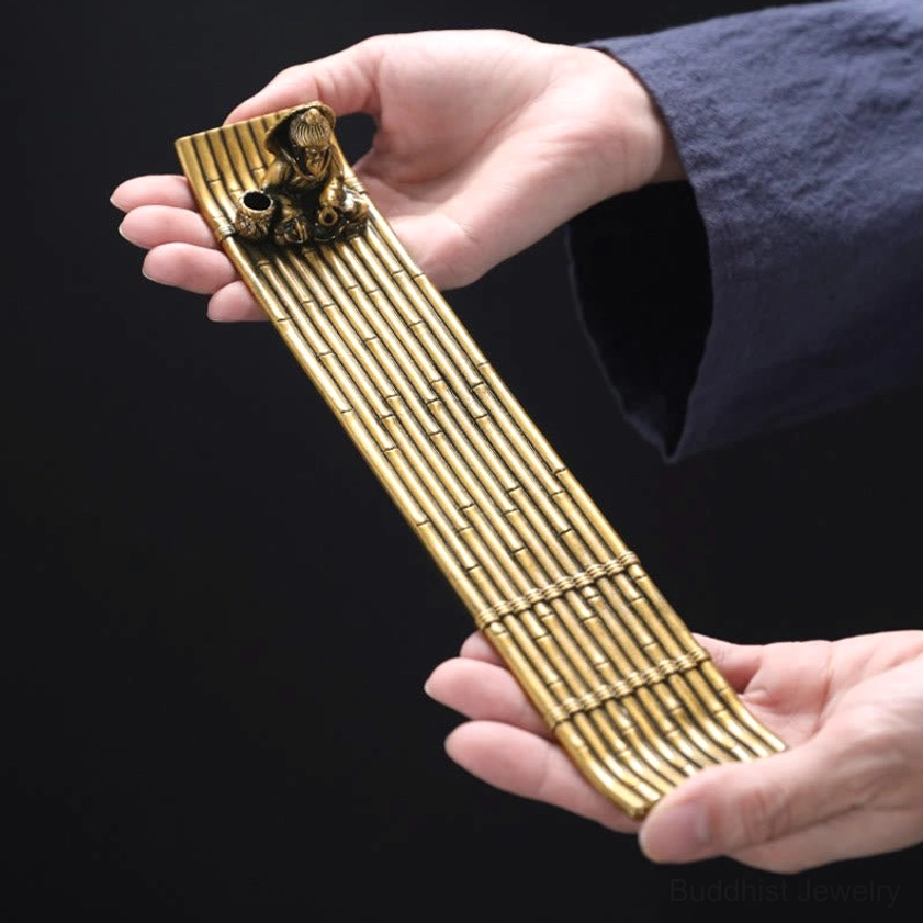 Hand-held side view of handcrafted bamboo raft incense holder with vintage brass tone and detailed bamboo joint design