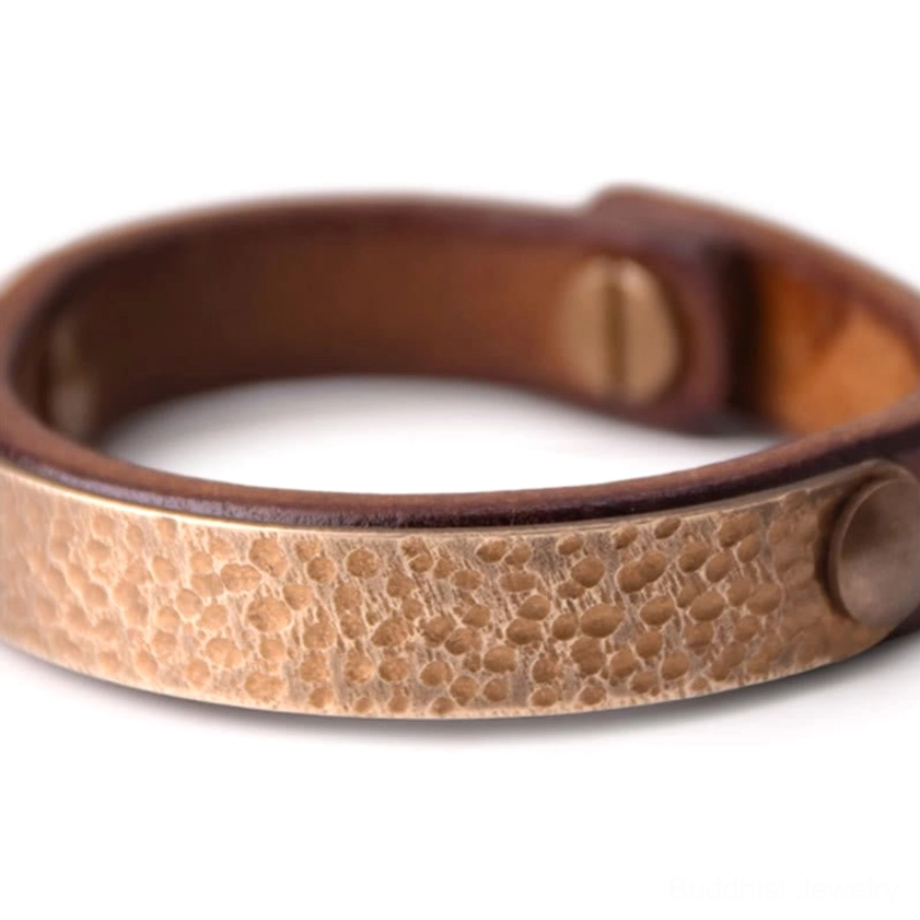 Close-up detail of textured hammered brass panel on leather Buddhist wealth bangle with visible rivet fasteners