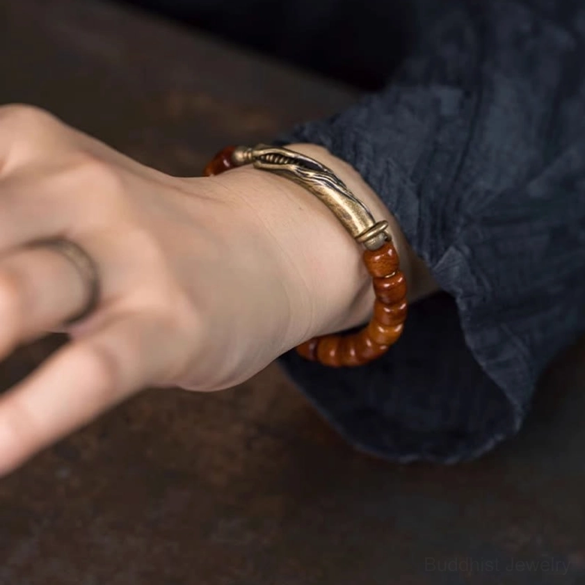 Bone beads strength bracelet styled on human hand in casual close-up, showing bronze metal clasp and brown cylinder beaded design against dark clothing