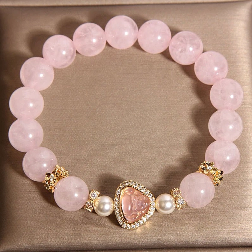 Full view of beaded Buddha bracelet direct top-down angle on brown jewelry tray with single Buddha charm centered among smooth pink crystal beads