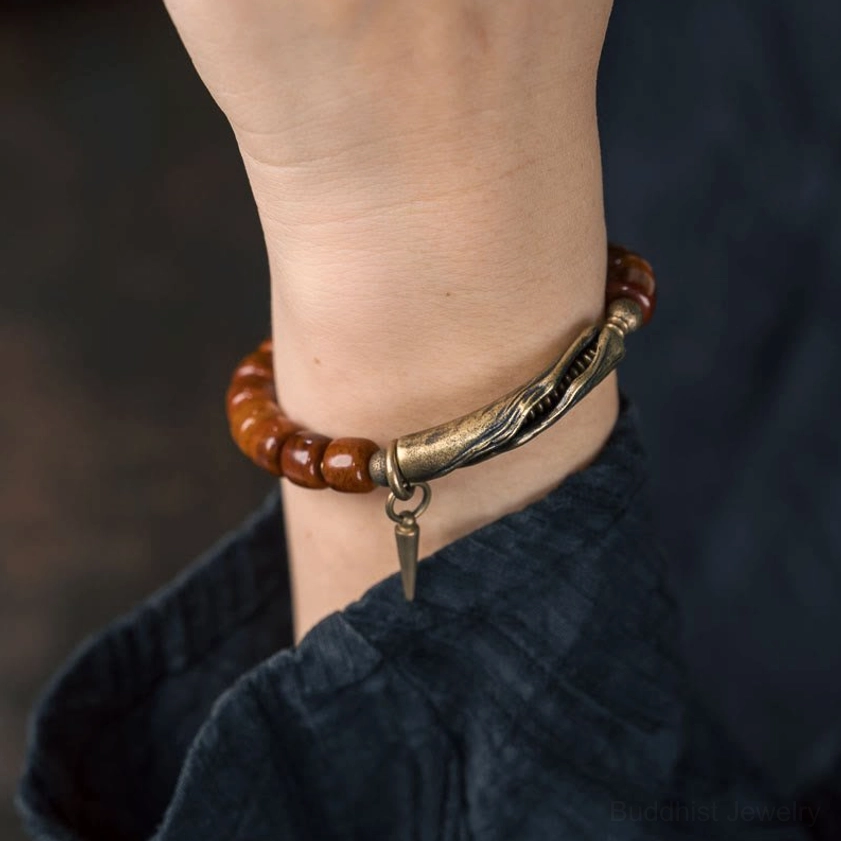 Spiritual strength bracelet worn on human wrist in close-up, showing brown bone-style beads, bronze hardware, and hanging spike charm against dark clothing