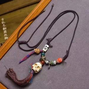 Handcrafted beige bone skull Buddhist protection necklace pendant with turquoise beads, agate, and colorful woven tassel on wooden display