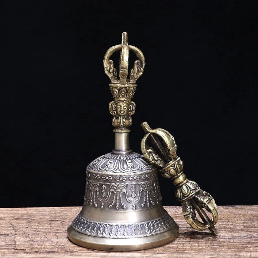 Tibetan meditation bell and vajra dorje set with Buddha head carvings on handle, resting on bamboo mat with linen background
