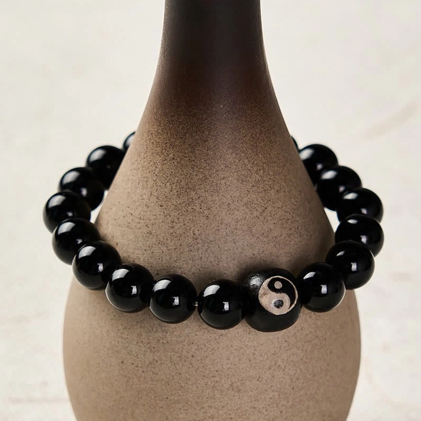 Black beaded bracelet with yin yang charm displayed on ceramic vase prop three quarter view