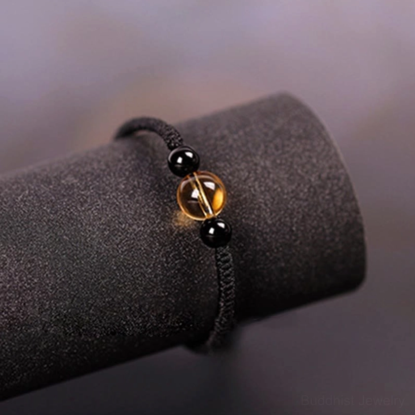 Close-up side view of black Buddhist bracelet with citrine flanked by obsidian beads on velvet