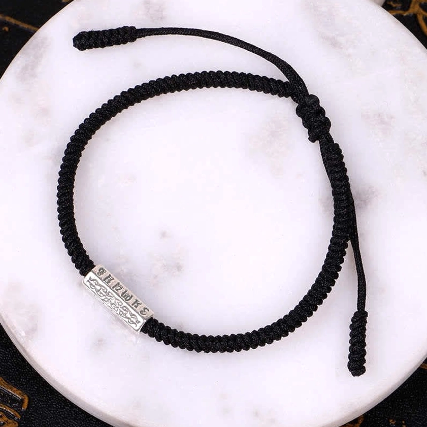 Black woven Om Mani Padme Hum Buddhist luck bracelet with engraved silver charm and braided rope with adjustable knot closure on marble plate background