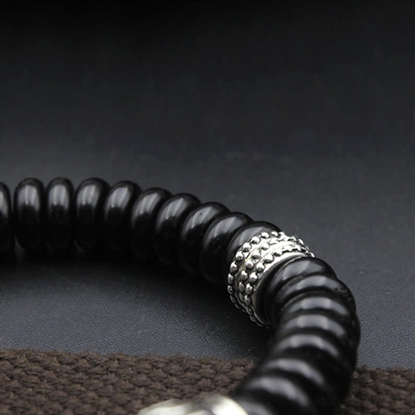 Partial close-up view of black coconut shell Buddhist bracelet with single silver metal spacer and dark woven fabric