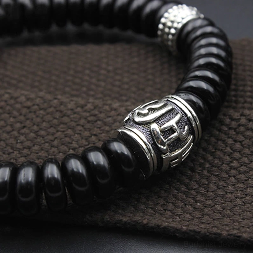 Close-up side view of black coconut shell Om Mani Padme Hum bracelet with large engraved silver barrel bead