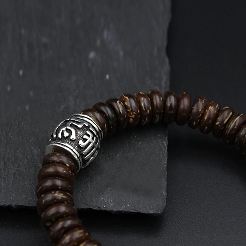 Black matte coconut shell bracelet with Sanskrit mantra charm and silver metal accents on brown leather background